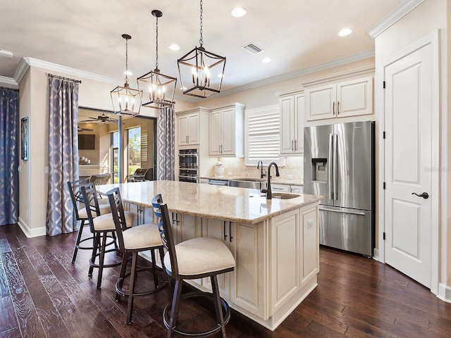 kitchen with pendant lighting, a kitchen island with sink, dark wood-type flooring, appliances with stainless steel finishes, and light stone countertops