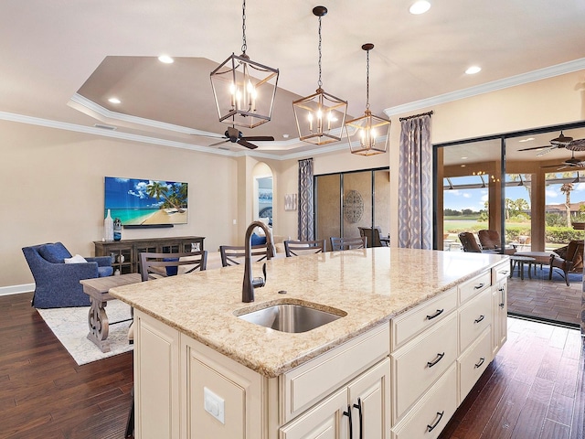 kitchen with an island with sink, light stone counters, sink, dark hardwood / wood-style flooring, and decorative light fixtures