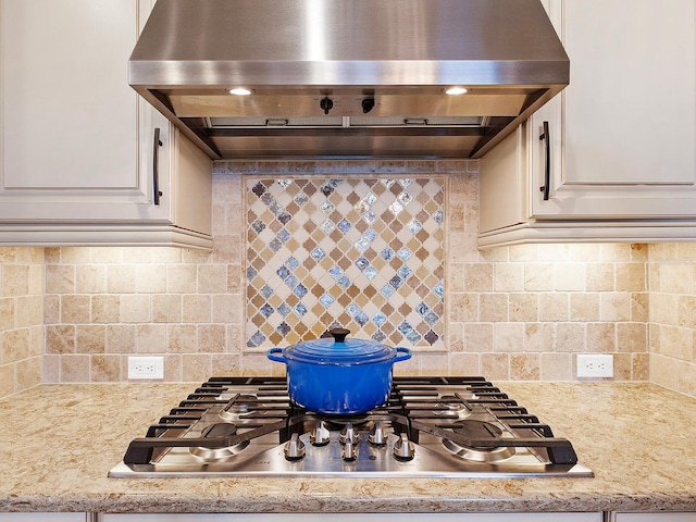 kitchen featuring wall chimney exhaust hood, light stone countertops, stainless steel gas cooktop, and tasteful backsplash