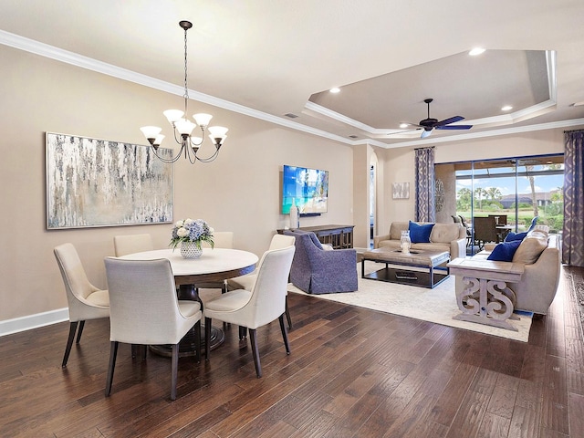 dining space featuring a raised ceiling, ceiling fan with notable chandelier, dark hardwood / wood-style floors, and ornamental molding