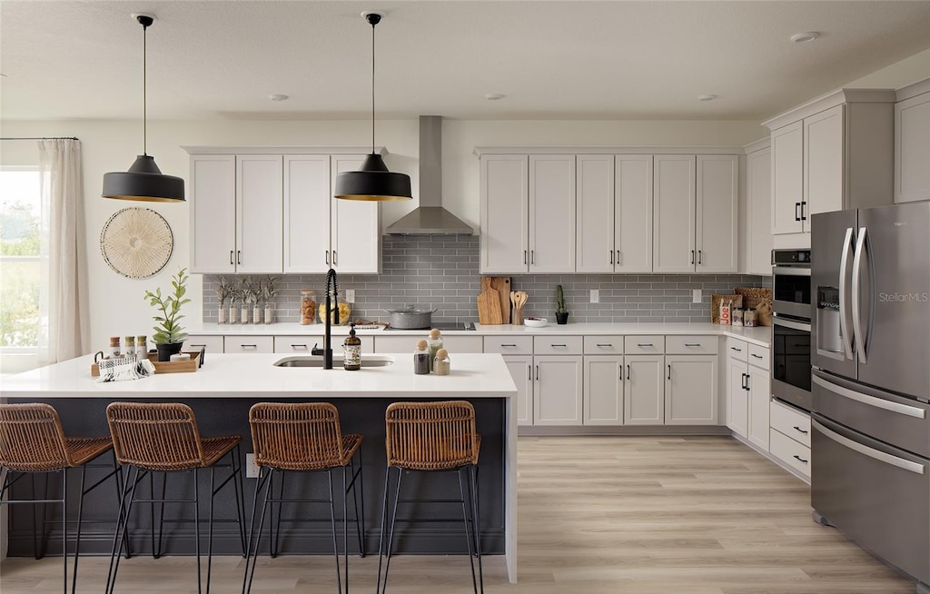 kitchen featuring appliances with stainless steel finishes, pendant lighting, wall chimney range hood, and white cabinetry