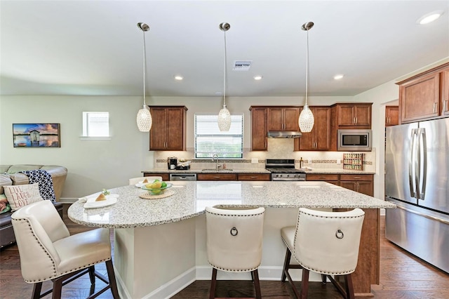 kitchen featuring a kitchen breakfast bar, stainless steel appliances, decorative light fixtures, a center island, and sink