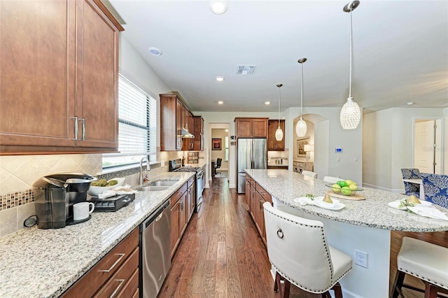 kitchen with stainless steel appliances, a breakfast bar, sink, light stone counters, and pendant lighting