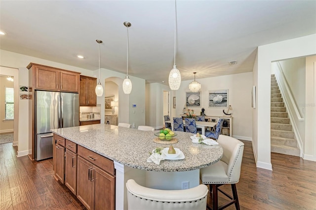 kitchen with hanging light fixtures, a breakfast bar area, stainless steel refrigerator, a center island, and dark hardwood / wood-style flooring