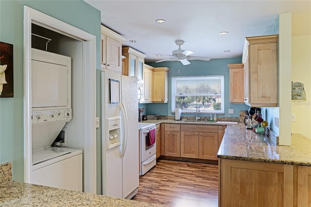 kitchen featuring stacked washer / dryer, sink, light hardwood / wood-style flooring, white appliances, and ceiling fan