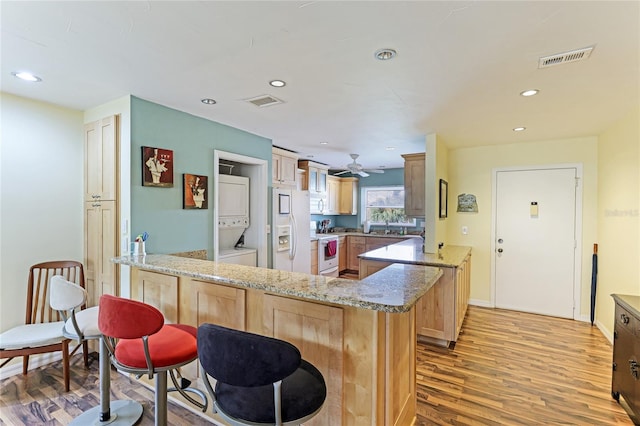 kitchen featuring white appliances, kitchen peninsula, light hardwood / wood-style floors, and stacked washer and clothes dryer