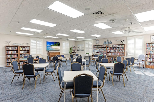 carpeted dining space with a paneled ceiling and ceiling fan