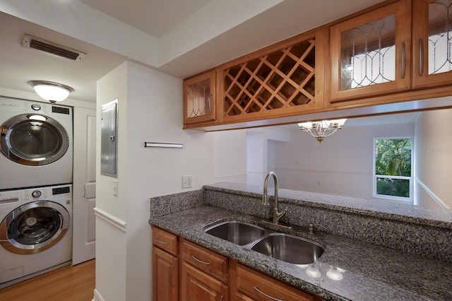 interior space featuring wet bar, stacked washer / dryer, light hardwood / wood-style flooring, electric panel, and a notable chandelier