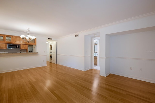 unfurnished living room featuring light wood-type flooring, a chandelier, crown molding, and stacked washing maching and dryer