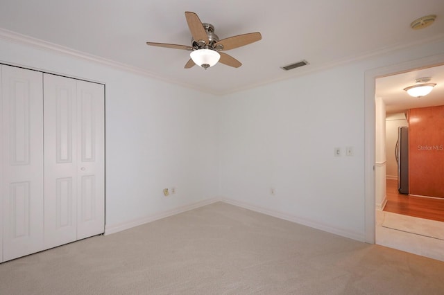 unfurnished bedroom with stainless steel fridge, a closet, ceiling fan, ornamental molding, and light colored carpet