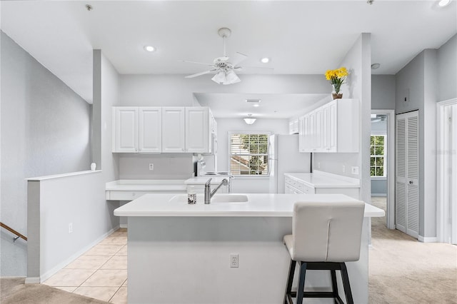 kitchen with a kitchen breakfast bar, white cabinets, white fridge, ceiling fan, and light colored carpet