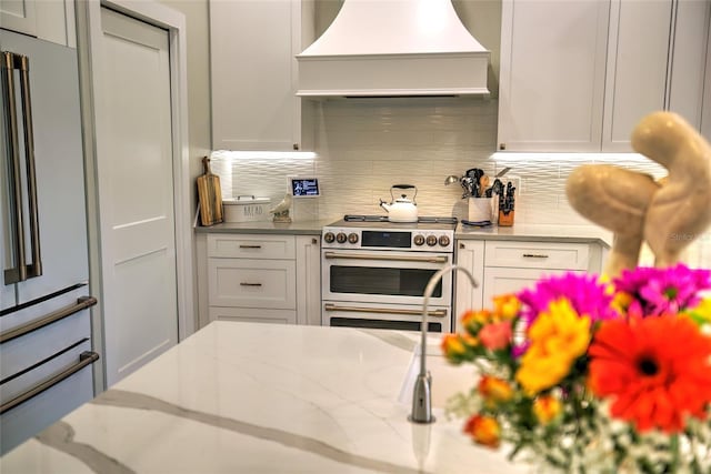 kitchen featuring backsplash, white cabinetry, custom range hood, stainless steel range, and white fridge