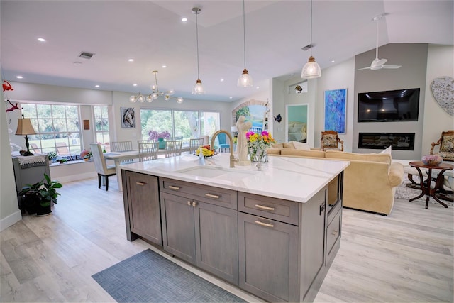 kitchen featuring sink, vaulted ceiling, light hardwood / wood-style flooring, decorative light fixtures, and light stone countertops