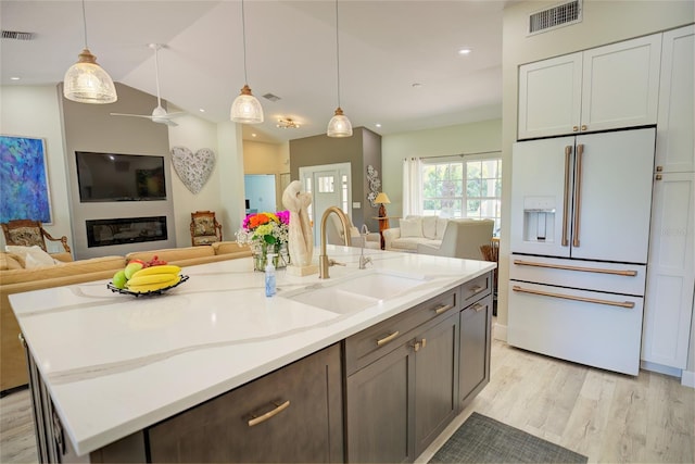 kitchen with pendant lighting, sink, a kitchen island with sink, white fridge with ice dispenser, and light wood-type flooring