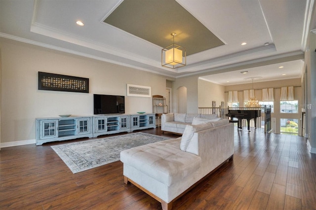 living room with a tray ceiling, dark wood-type flooring, a chandelier, and crown molding