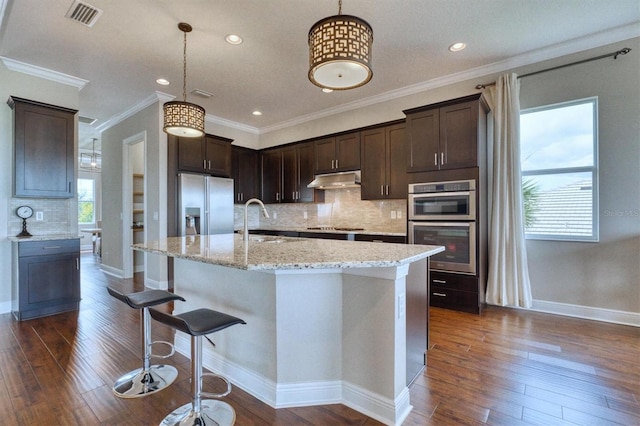 kitchen with appliances with stainless steel finishes, decorative light fixtures, sink, and an island with sink