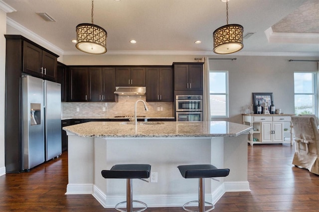 kitchen featuring stainless steel appliances, a kitchen island with sink, light stone countertops, and pendant lighting