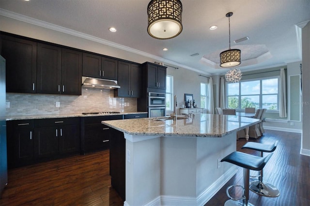 kitchen with a kitchen island with sink, dark hardwood / wood-style flooring, appliances with stainless steel finishes, a kitchen bar, and pendant lighting