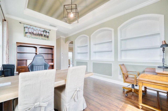 dining area featuring a tray ceiling, wood-type flooring, crown molding, and built in shelves