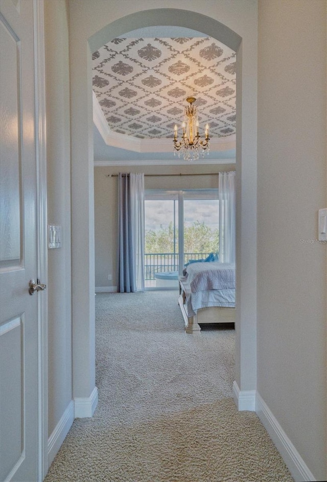 hallway with a chandelier, a raised ceiling, and carpet