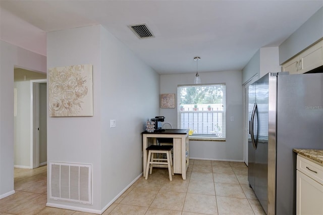 kitchen featuring hanging light fixtures, stainless steel refrigerator, light tile patterned floors, and light stone counters