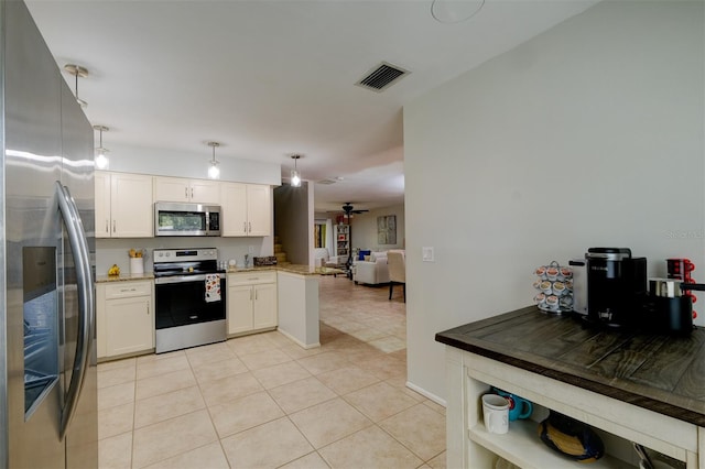 kitchen with white cabinets, kitchen peninsula, light tile patterned floors, stainless steel appliances, and decorative light fixtures