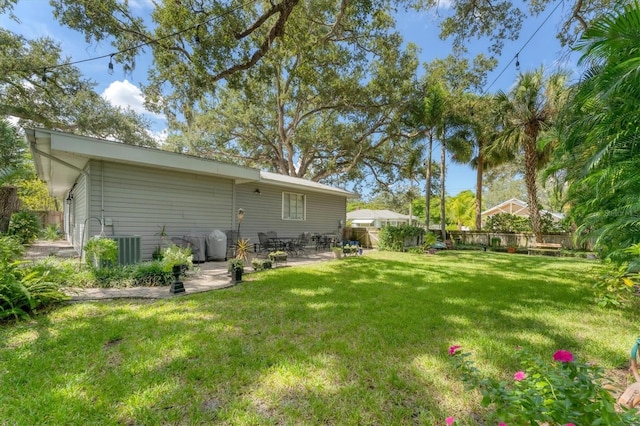rear view of house with central AC unit, fence, a lawn, and a patio area