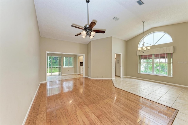 unfurnished room featuring ceiling fan with notable chandelier, light hardwood / wood-style floors, lofted ceiling, and a healthy amount of sunlight