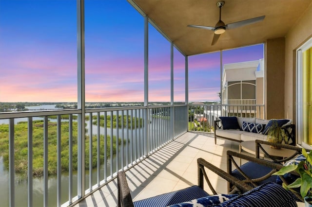 balcony at dusk featuring a water view and a ceiling fan