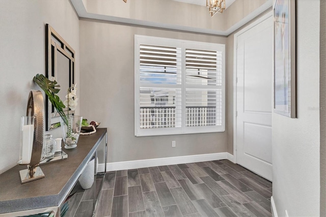doorway with baseboards, a chandelier, and wood finish floors