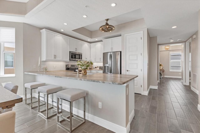 kitchen with kitchen peninsula, tasteful backsplash, white cabinetry, stainless steel appliances, and a kitchen breakfast bar