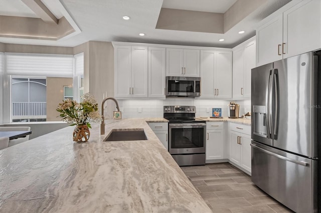 kitchen featuring light stone countertops, a sink, a raised ceiling, white cabinets, and appliances with stainless steel finishes