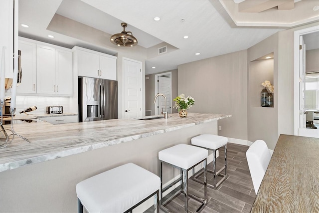 kitchen featuring light stone counters, a raised ceiling, sink, white cabinetry, and stainless steel appliances