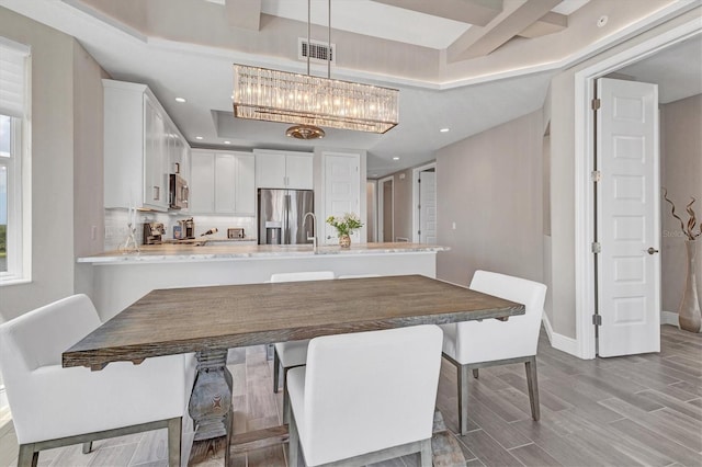 dining room with a raised ceiling, light hardwood / wood-style flooring, and sink