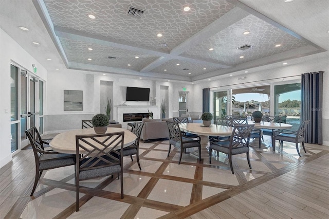 dining room featuring coffered ceiling, a glass covered fireplace, french doors, and visible vents