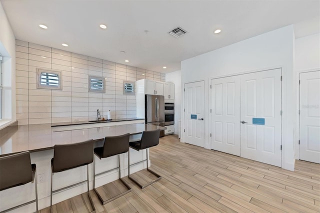 kitchen featuring freestanding refrigerator, visible vents, a sink, a kitchen bar, and white cabinets