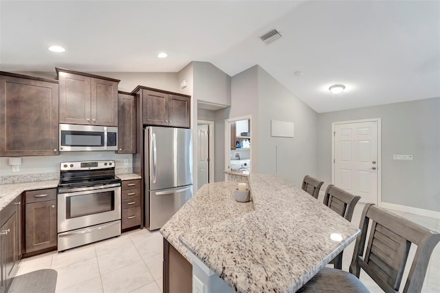 kitchen featuring appliances with stainless steel finishes, vaulted ceiling, a kitchen island, and light stone counters