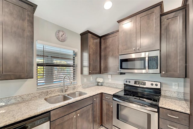 kitchen featuring appliances with stainless steel finishes, dark brown cabinetry, light stone counters, and sink