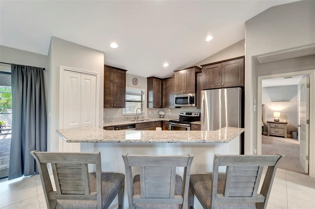 kitchen featuring light stone countertops, stainless steel appliances, vaulted ceiling, light tile patterned floors, and a kitchen island