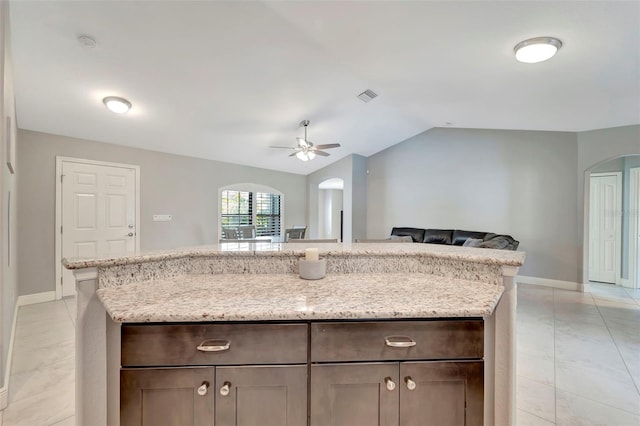 kitchen featuring vaulted ceiling, ceiling fan, light stone countertops, light tile patterned floors, and dark brown cabinetry