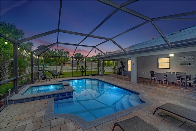 pool at dusk featuring glass enclosure, an in ground hot tub, and a patio