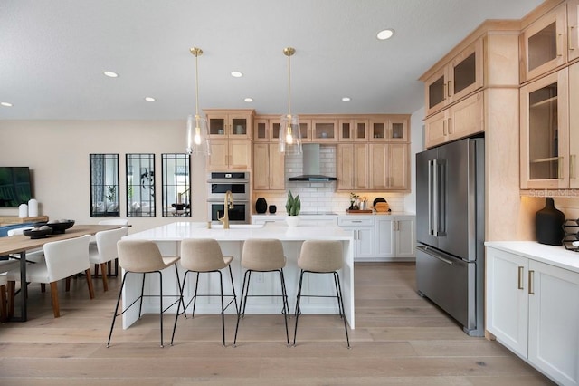 kitchen with wall chimney exhaust hood, hanging light fixtures, an island with sink, and stainless steel appliances