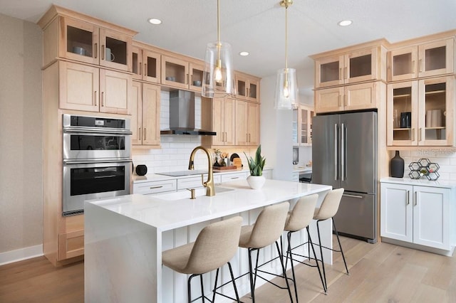 kitchen featuring a center island with sink, wall chimney exhaust hood, hanging light fixtures, backsplash, and appliances with stainless steel finishes