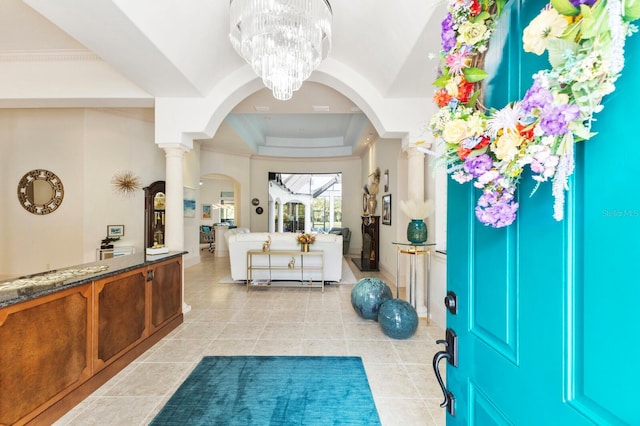 entrance foyer with ornate columns, a raised ceiling, a notable chandelier, crown molding, and light tile patterned floors