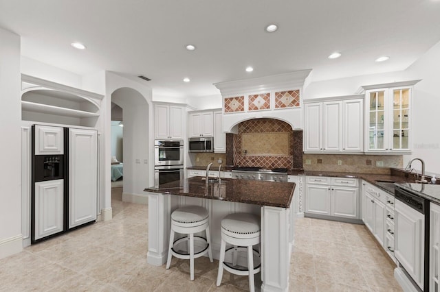 kitchen with white cabinetry, sink, stainless steel appliances, dark stone counters, and a center island with sink