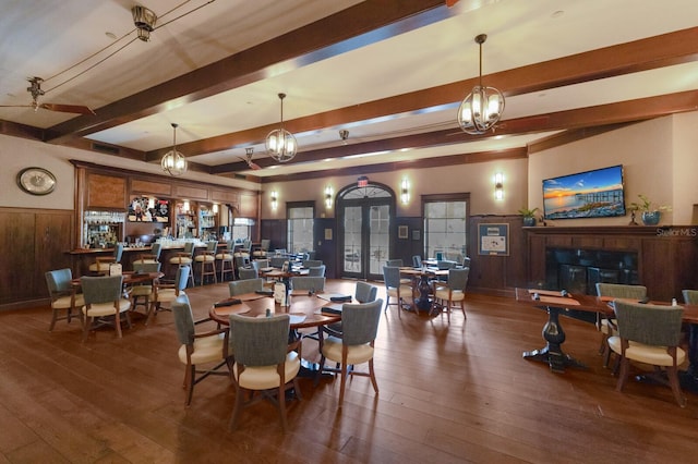 dining room with beamed ceiling, dark wood-type flooring, wooden walls, and french doors