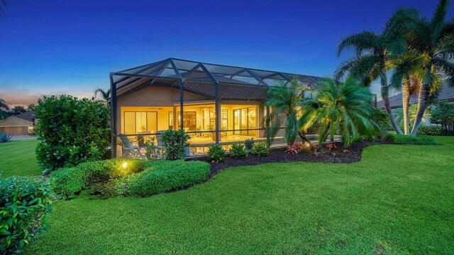 back house at dusk featuring glass enclosure and a yard