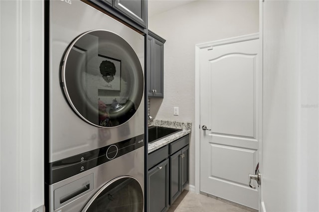 washroom featuring cabinets, stacked washing maching and dryer, light tile patterned flooring, and sink