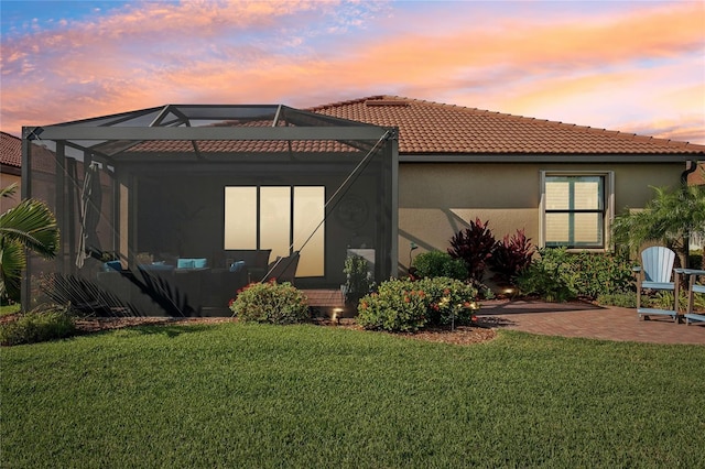 back house at dusk featuring a lanai, a patio area, and a yard