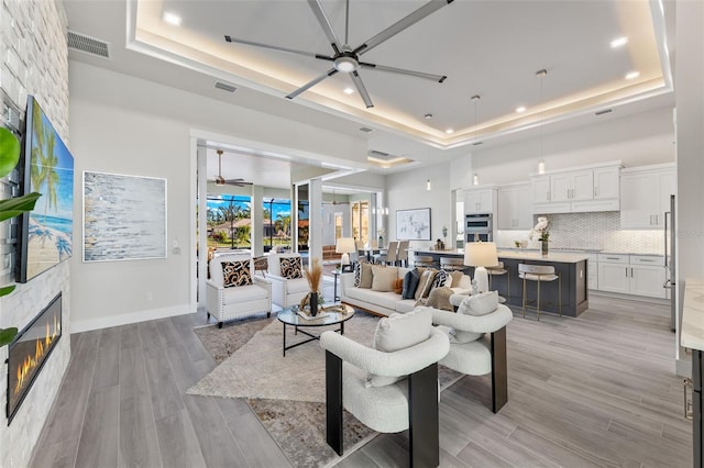 living room featuring ceiling fan, a fireplace, light hardwood / wood-style floors, and a raised ceiling